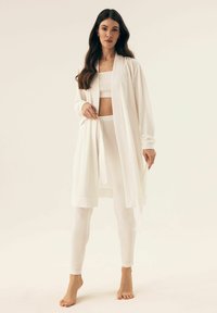 Biała, długoslepowa odzież w stylu kimono w połączeniu z białym, prążkowanym crop topem i legginsami, prezentująca miękki, teksturowany materiał.