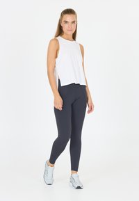 Top bianco senza maniche con spacchi laterali, abbinato a leggings blu navy. Il modello indossa scarpe da ginnastica grigie chiare con dettagli neri.