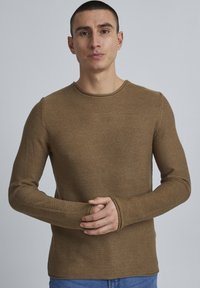Maglietta a maniche lunghe marrone a coste realizzata in tessuto a maglia testurizzato con colletto rotondo. Presenta maniche aderenti e fori per il pollice per un comfort aggiuntivo.