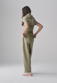 Top aderente verde oliva con scollo casual drappeggiato, abbinato a pantaloni larghi verde oliva e morbide scarpe slip-on rosa tenue.