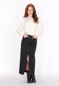 Witte lange mouwen top met pofmouwen, gecombineerd met een zwarte denim maxi rok met een hoge split en zwart kniehoge laarzen.
