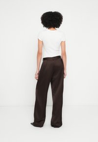 T-shirt blanc à manches courtes associé à un pantalon ample en satin marron foncé, avec une ceinture à la taille et un tissu fluide et lisse.