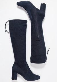 Marinblå mocka stövlar som går över knäna med en kraftig klack, sidodragkedjedetalj och snörning upptill för justerbar passform.