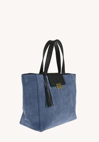 Sac fourre-tout en cuir suédé bleu avec des poignées en cuir noir, un rabat en cuir noir avec un fermoir en or, et un détail en pompon noir.