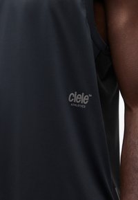 Gros plan sur une personne portant un débardeur noir de Ciele Athletics, montrant le bras et le logo sur la poitrine.