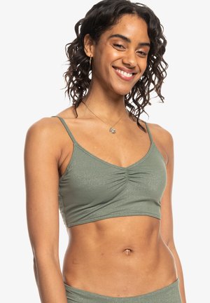 Bralette verde chiaro con spalline regolabili, dettaglio centrale arricciato e una texture morbida, leggermente lucida. Adatto per essere indossato a strati o per un look casual.