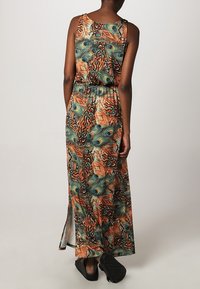 Robe maxi avec un motif vibrant de plumes de paon en vert, orange et bleu, avec une taille cintrée et une fente sur le côté ; tissu léger.