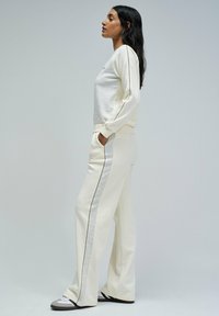 Conjunto de sudadera blanco que presenta una parte superior texturizada y pantalones suaves con una franja lateral. La tela es suave, con un corte holgado y bolsillos en los pantalones.
