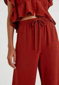 Roestkleurige, lichtgewicht katoenen blouse met ruches op de mouwen en een knoopsluiting, gecombineerd met bijpassende relaxte broek met een trekkoord in de taille.