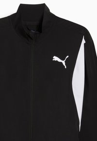 Sort træningsjakke med høj krave, hvide sideakkorder og et fremtrædende hvidt Puma-logo på venstre bryst. Glat stofstruktur.