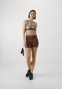 Reggiseno sportivo con motivo zebra bianco e nero, abbinato a pantaloni corti a strisce tigre arancioni e neri; in mano una corda per saltare; indossa sneaker nere.