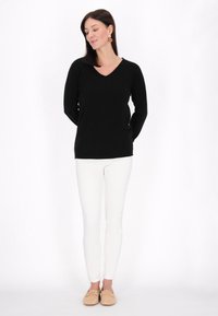 Pulover negru din tricot cu mânecă lungă și decolteu în V, asociat cu blugi skinny albi și pantofi slip-on bej. Design simplu, textură netedă.