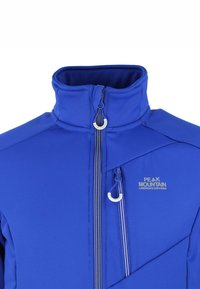 Blauwe softshell jas met hoge kraag, contrasterende witte ritsen, logo op de borst en diagonale naaddetails; gladde textuur.