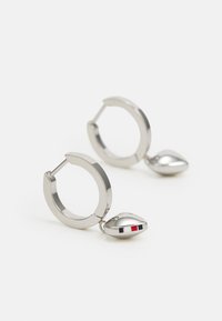 Pendientes de aro de plata con una textura suave. Cada uno presenta un charm en forma de lágrima con acentos en rojo, blanco y azul. Diseño moderno.