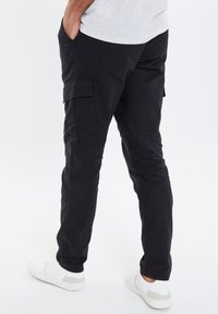 Zwarte cargo pants met een slim fit, voorzien van zijzakken en een soepele textuur. Draag ze met witte sneakers, wat zorgt voor een casual stijl.