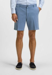 Light blue cotton shorts with a smooth texture, featuring a button closure, side pockets, and a clean hem. Paired with black slip-on shoes.