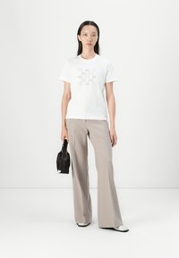 Weißes Baumwoll-T-Shirt mit grafischem Druck, kombiniert mit hellbeigen, weiten Hosen und einer kleinen schwarzen Handtasche. Model trägt minimalistische Schuhe.