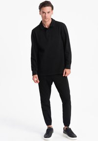 Sort langærmet polo skjorte parret med sorte tætsiddende bukser og mørke sneakers. Glat stof, afslappet pasform og diskrete syninger.