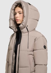 Beżowa kurtka puchowa z dużym, kapturkiem, zapięciem na zamek z przodu, regulowanymi sznurkami oraz bocznymi kieszeniami. Gładka, pikowana tekstura.