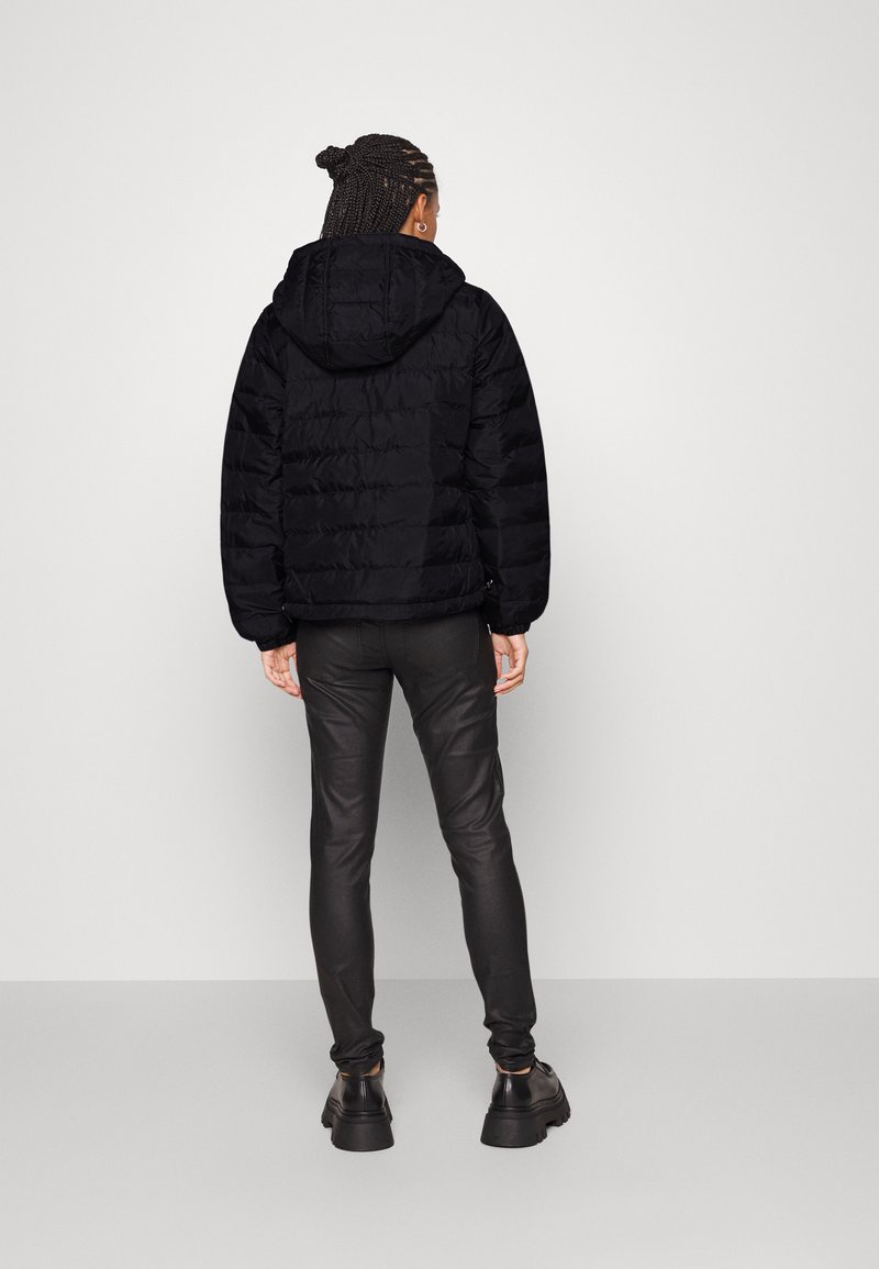 Doudoune noire avec capuche, dotée de coutures horizontales, de poignets élastiques et d'une coupe décontractée. Associée à un pantalon slim noir et des chaussures massives.