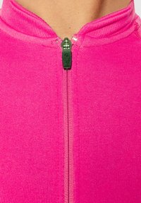 Aansluitend roze zip-up kledingstuk met een hoge kraag, voorzien van een zwarte ritsring. Het materiaal heeft een gladde, gestructureerde afwerking.