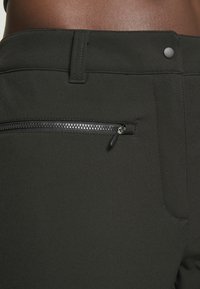 Pantalones elásticos negros que cuentan con un bolsillo lateral con cremallera, textura de tela suave y un diseño ajustado con un cierre de botón en la cintura.