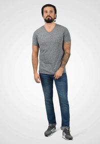 Grå v-hals t-skjorte laget av mykt stoff, kombinert med blå jeans og grå trening sko med sorte og hvite detaljer.