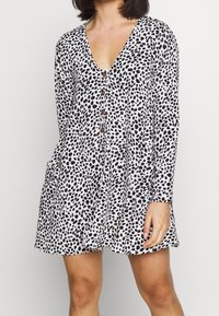 Šaty s leopardím potiskem v černobílé barvě, dlouhé rukávy, výstřih do V, zapínání na knoflíky vpředu a boční kapsy. Lehká, splývavá tkanina.