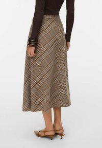 Femme portant une jupe midi à carreaux marron, un haut à manches longues marron, des chaussures marron à talons bas et des bracelets foncés, vue de dos.