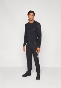 Juodas ilgomis rankovėmis marškinėliai su "Sweet Protection" logotipu, derinami su juodomis keln�ėmis, turinčiomis baltus akcentus. Tekstūruotas audinys, prigludęs dizainas.