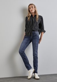 Svart och vit randig skjorta med knappar, långa ärmar, matchad med mörkblå slim-fit jeans och vita sneakers med bruna detaljer.