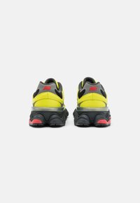 Black and yellow athletic shoes feature a textured upper, rear accents in grey and red, and a wavy black sole with red highlights.