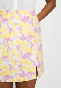 Jupe pour femme avec motif floral abstrait jaune et rose et une fente à l'avant, associée à un top blanc côtelé.
