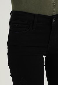 Jeans de denim negro con un ajuste slim, que presentan un bolsillo frontal, detalle desgastado en la rodilla y sutiles acentos de costura.