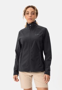 Zwarte softshell jas met een hoge kraag, een frontale rits en zijzakken. Heeft een strak ontwerp en minimale branding op de borst.