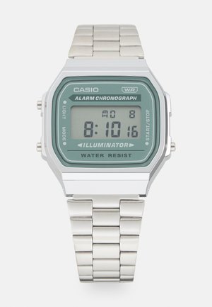 Skaitmeninis „Casio“ laikrodis su stačiakampiu žaliu ciferblatu, nerūdijančio plieno juosta ir sidabrinėmis detalėmis; turi skaitmeninį ekraną ir kelis funkcijų mygtukus.