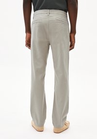 Pantaloni dritti grigio chiaro con una tessitura liscia, passanti per cintura e due tasche posteriori, abbinati a scarpe beige senza lacci.