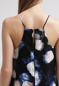 Svart blommig topp med tunna axelband och en nyckelhålsöppning i ryggen. Tyget har en slät textur med stora rosa och blå blommönster.