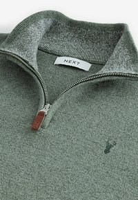 Svijetlozeleni dukserica s patentnim zatvaračem i mekanom teksturom, s kontrastnim sivim ovratnikom, metalnim patentnim zatvaračem i malim logom jelena na prsima. Brand oznaka: NEXT.