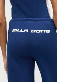 Κοντινό πλάνο ενός ατόμου που φορά μπλε παντελόνια με λευκό κείμενο «Billabong» στη πίσω μέση.