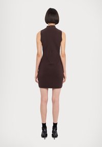 Brun ärmlös klänning med hög krage, figursydd passform, bakre sömdetaljer och en dold dragkedja, tillsammans med ankelstövlar.