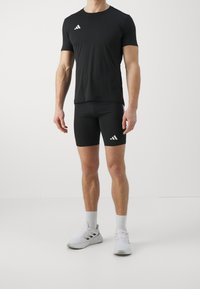 Camiseta deportiva negra de manga corta con logo blanco, combinada con pantalones cortos de compresión negros con un acento blanco. Zapatillas deportivas blancas completan el conjunto.