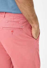 Pantaloni in cotone rosa con una singola tasca posteriore con chiusura a bottone, tasche laterali e un piccolo etichetta del marchio sul retro.