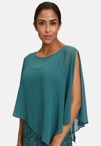 Poncho en chiffon teal avec une coupe ample, un décolleté arrondi et des côtés ouverts, associé à une jupe en dentelle texturée d'une couleur similaire.