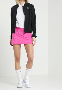 Zwarte bomberjack, witte polo en roze sportrok. Witte kniekousen en witte sneakers. Gladde stof met een aansluitend ontwerp.