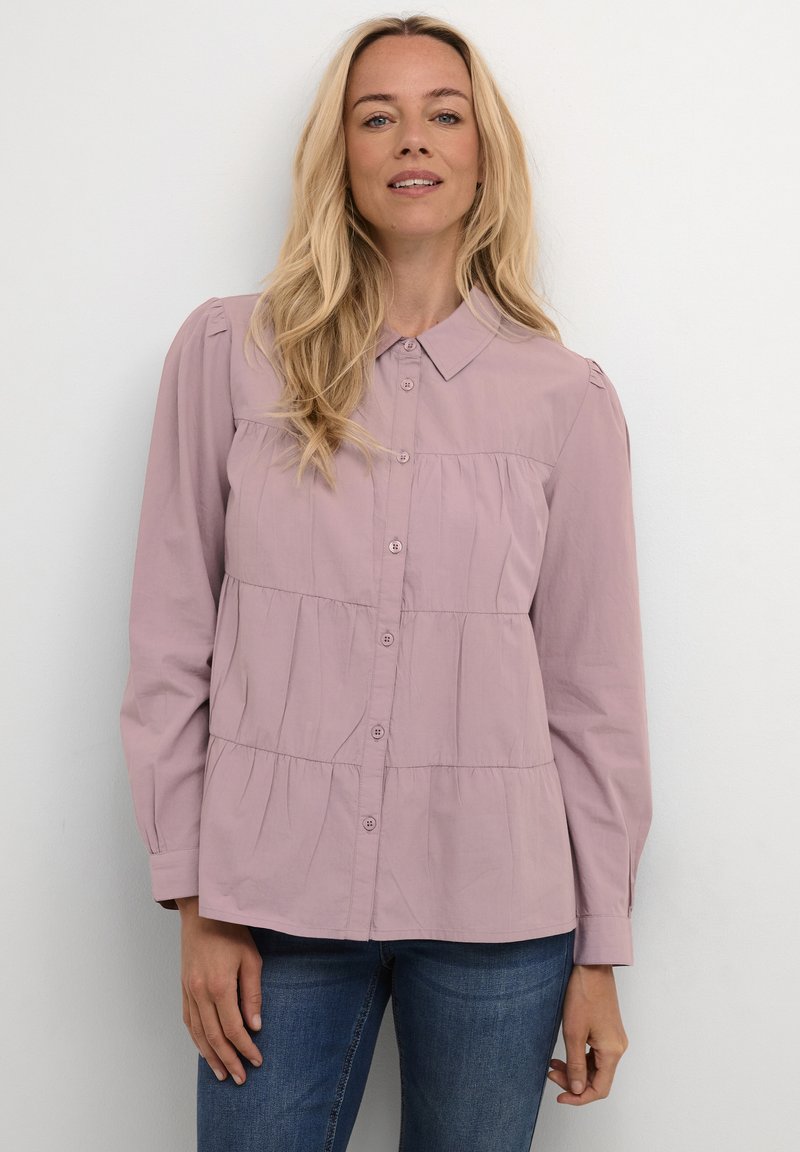 Camicia botton-down di colore lilla chiaro con colletto, caratterizzata da un design a strati e maniche lunghe. Tessuto liscio con sottili dettagli arricciati.
