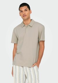 Lys grå polo shirt med et tekstureret mønster, korte ærmer og knaplukning, parret med stribede, lyse bukser.
