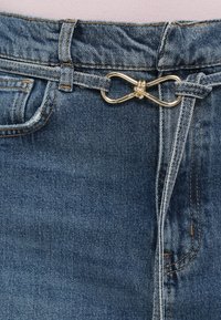 Denim šorti ar zilu mazgāšanu, zelta bezgalības formas sprādzi, parastajām jostām un redzamām šuvēm sānos un kabatās.