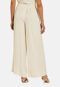 Lichte, crèmekleurige broek met een brede pijp en een elastische tailleband. De gestructureerde stof valt soepel en biedt een comfortabele pasvorm.