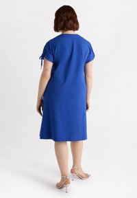 Niebieska sukienka z krótkim rękawem i detalami ze sznurkiem. Długość do połowy uda o luźnym kroju. W połączeniu z srebrnymi sandałami na obcasie.